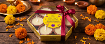 A gift-wrapped box of diyas tied with ribbon placed on a table with marigold flowers for Diwali gifting