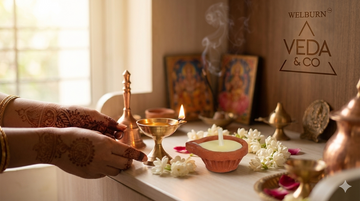 Hands lighting a diya for morning pooja ritual with incense and flowers — Veda & Co