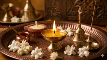 Traditional handcrafted diya lit for pooja ceremony with flowers and puja thali in background — Veda & Co