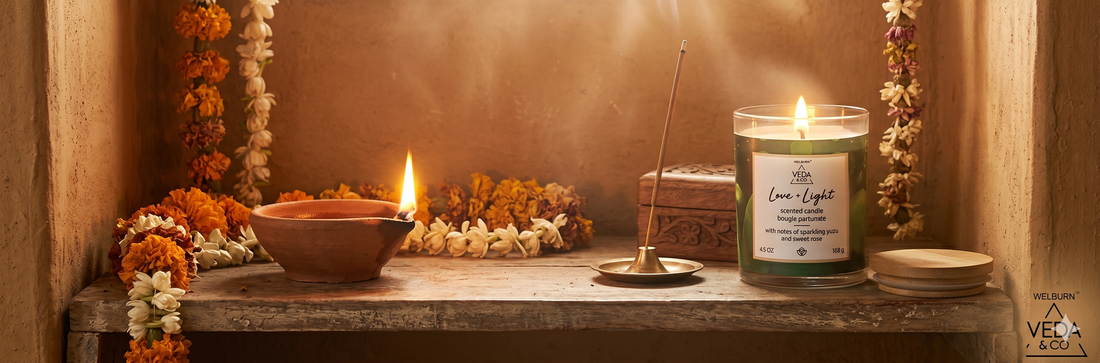 A clay ghee diya and a Veda & Co wellness candle burning side by side on a puja shelf in an Indian home